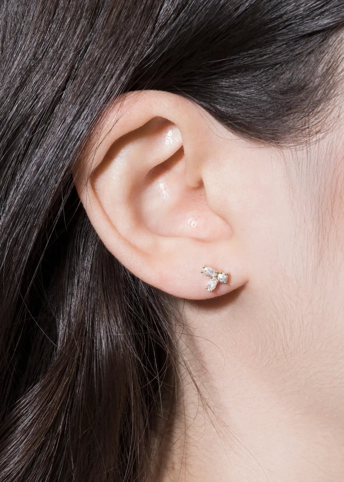 Close-up of a person's ear wearing delicate earrings, featuring sparkling stones, showcasing elegant jewelry.