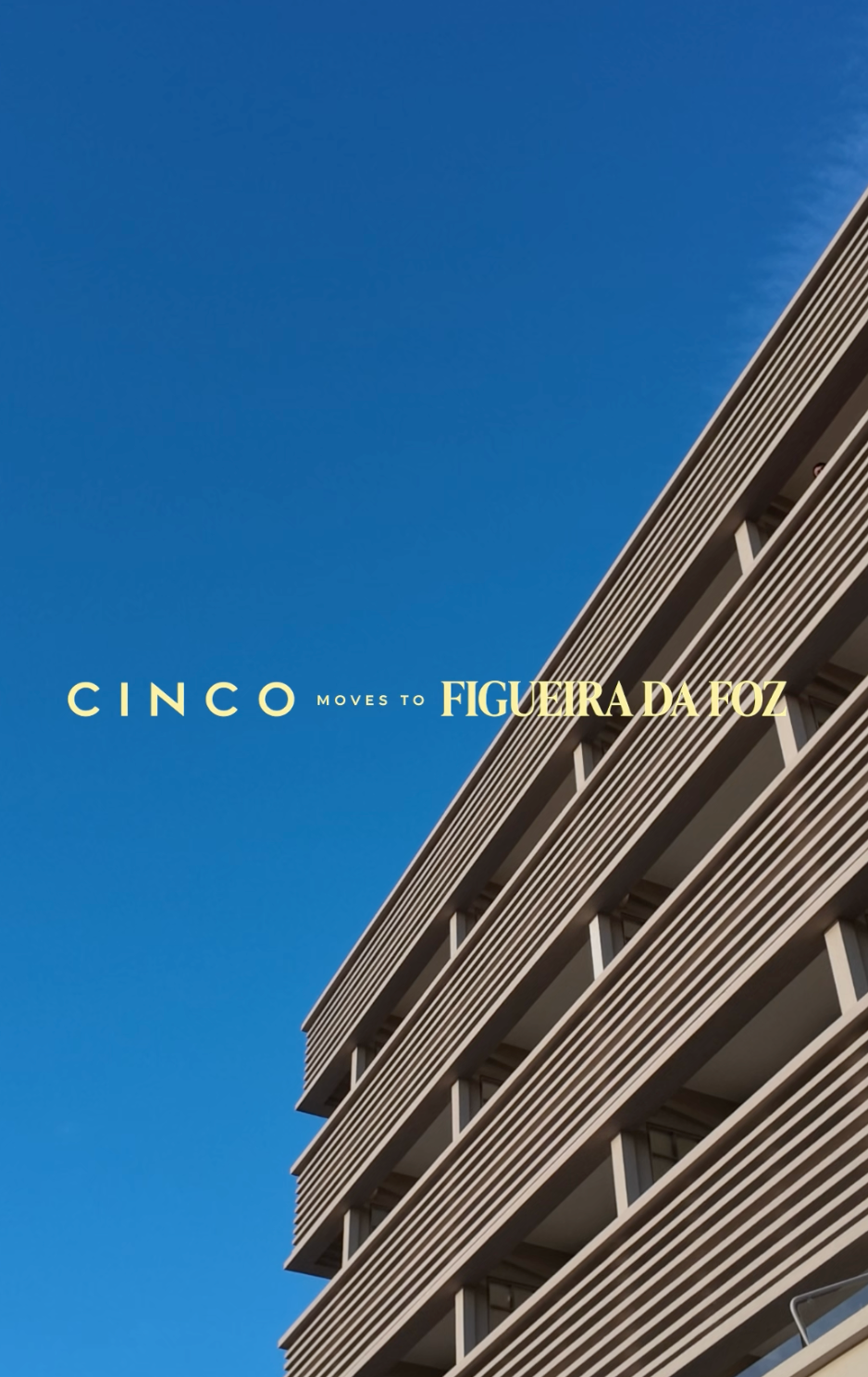 A modern multi-story building with horizontal slatted balconies photographed from a low angle against a clear blue sky. Text across the center reads 'CINCO MOVES TO FIGUEIRA DA FOZ' in pale yellow/gold lettering.