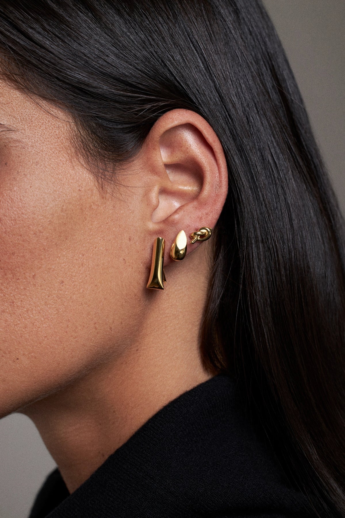 CINCO gold earrings worn on ear, featuring modern shapes with a polished finish.