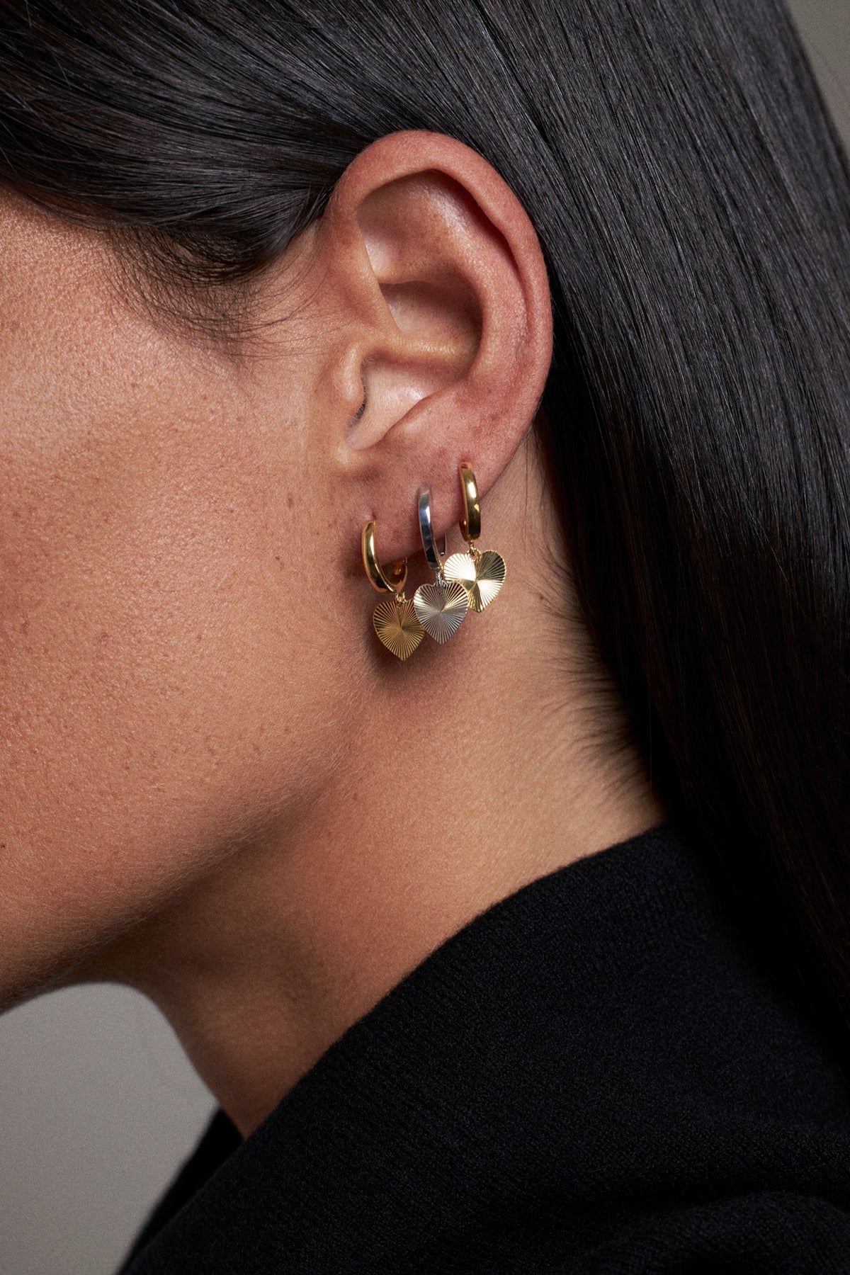 CINCO heart-shaped earrings worn on ear, featuring gold and silver finishes.
