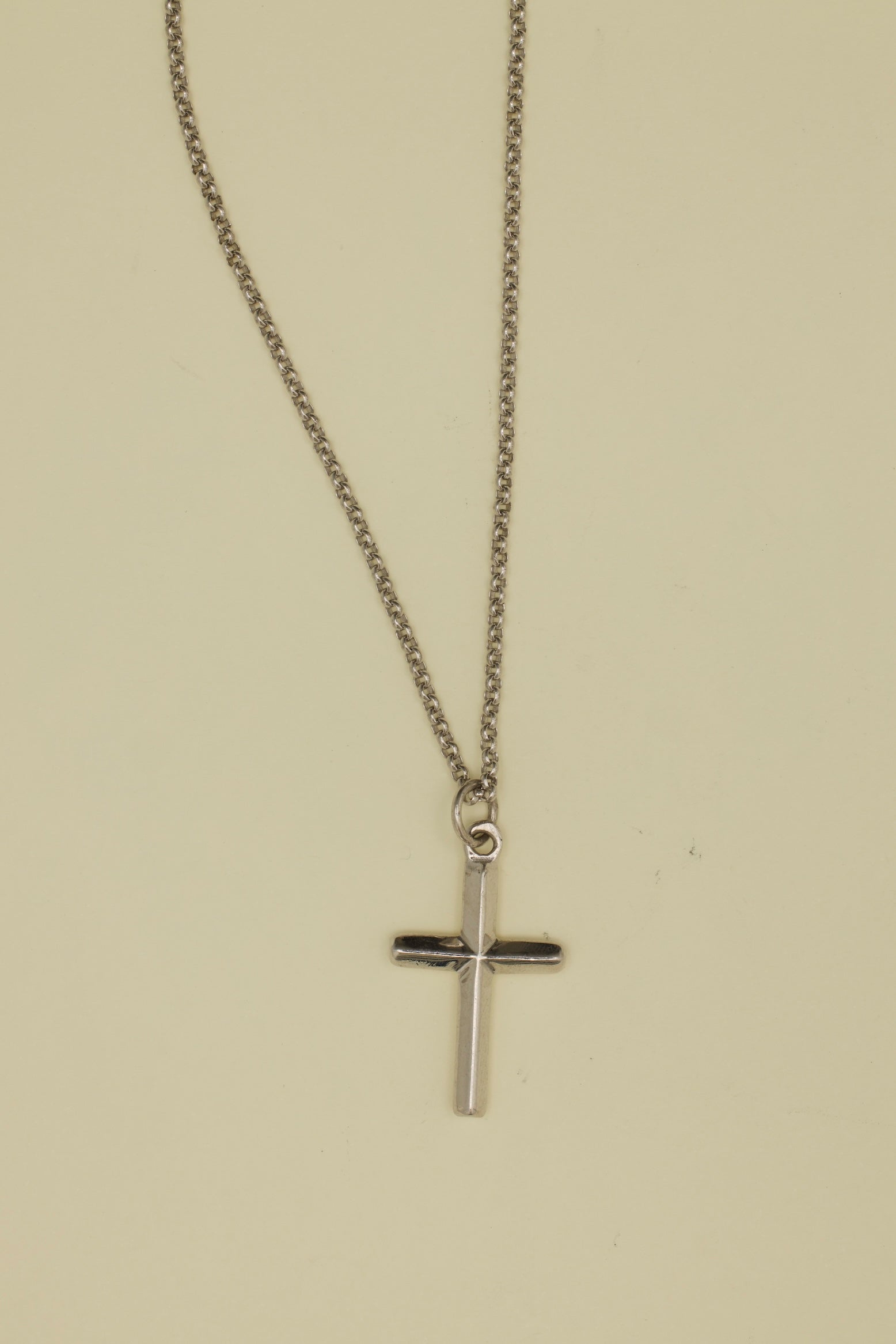 Silver cross necklace on a beige background