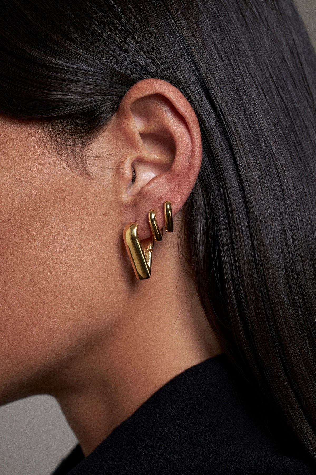 CINCO ear cuff earring in gold, worn on ear, showcasing a modern design with three delicate layers.