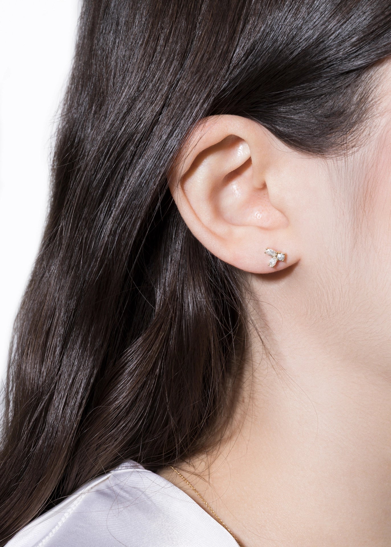 Close-up of an ear wearing a small earring with dark hair and a light background