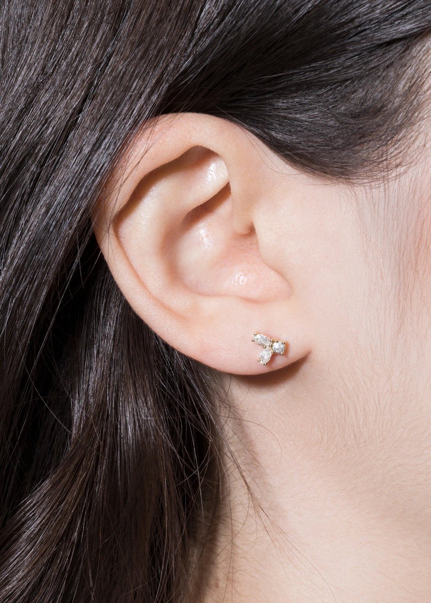 Close-up of an ear wearing a diamond stud earring with dark hair.