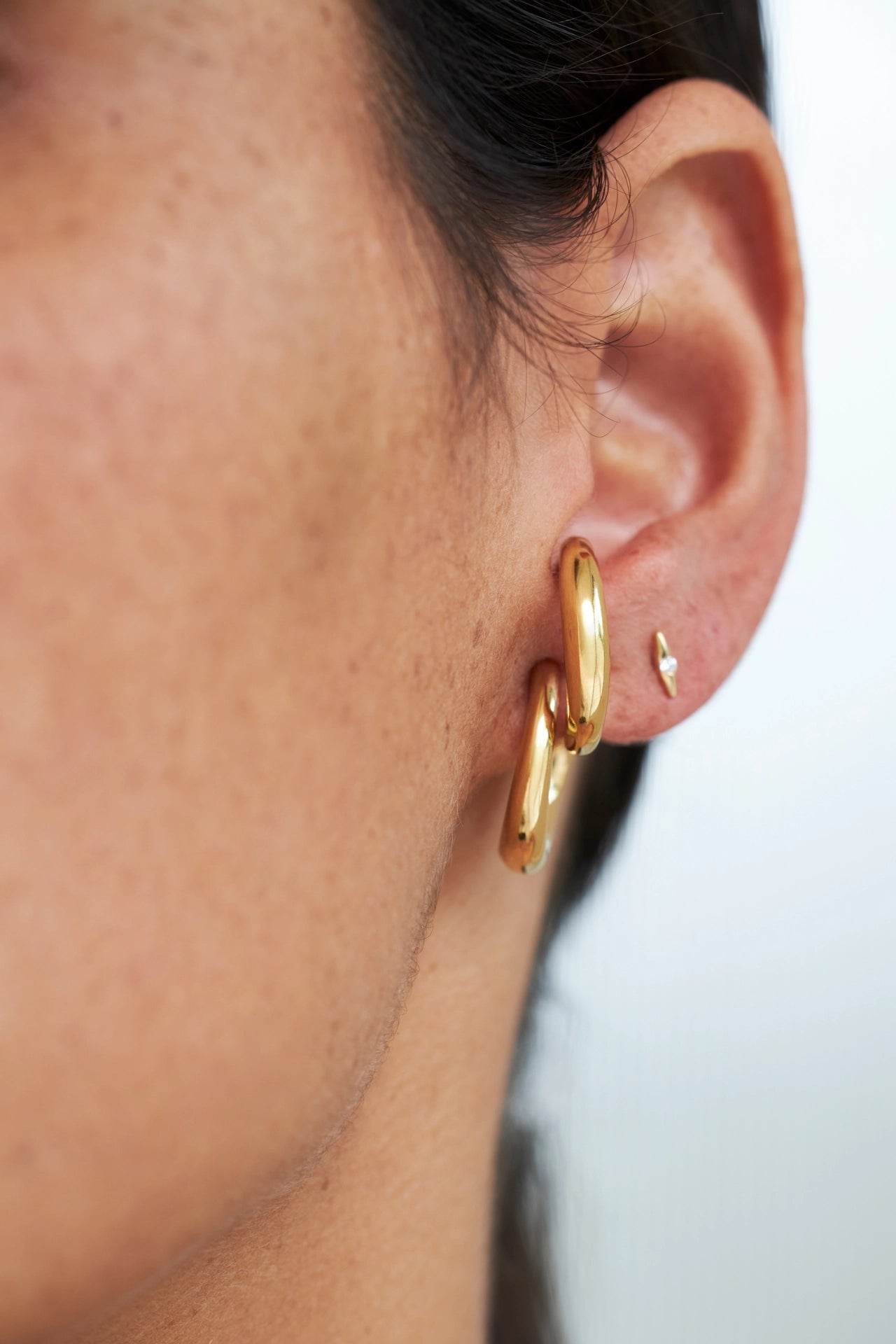 Close-up of an ear wearing gold hoop earrings with a blurred background