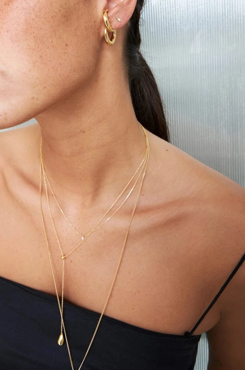 Woman wearing gold earrings and a necklace against a neutral background