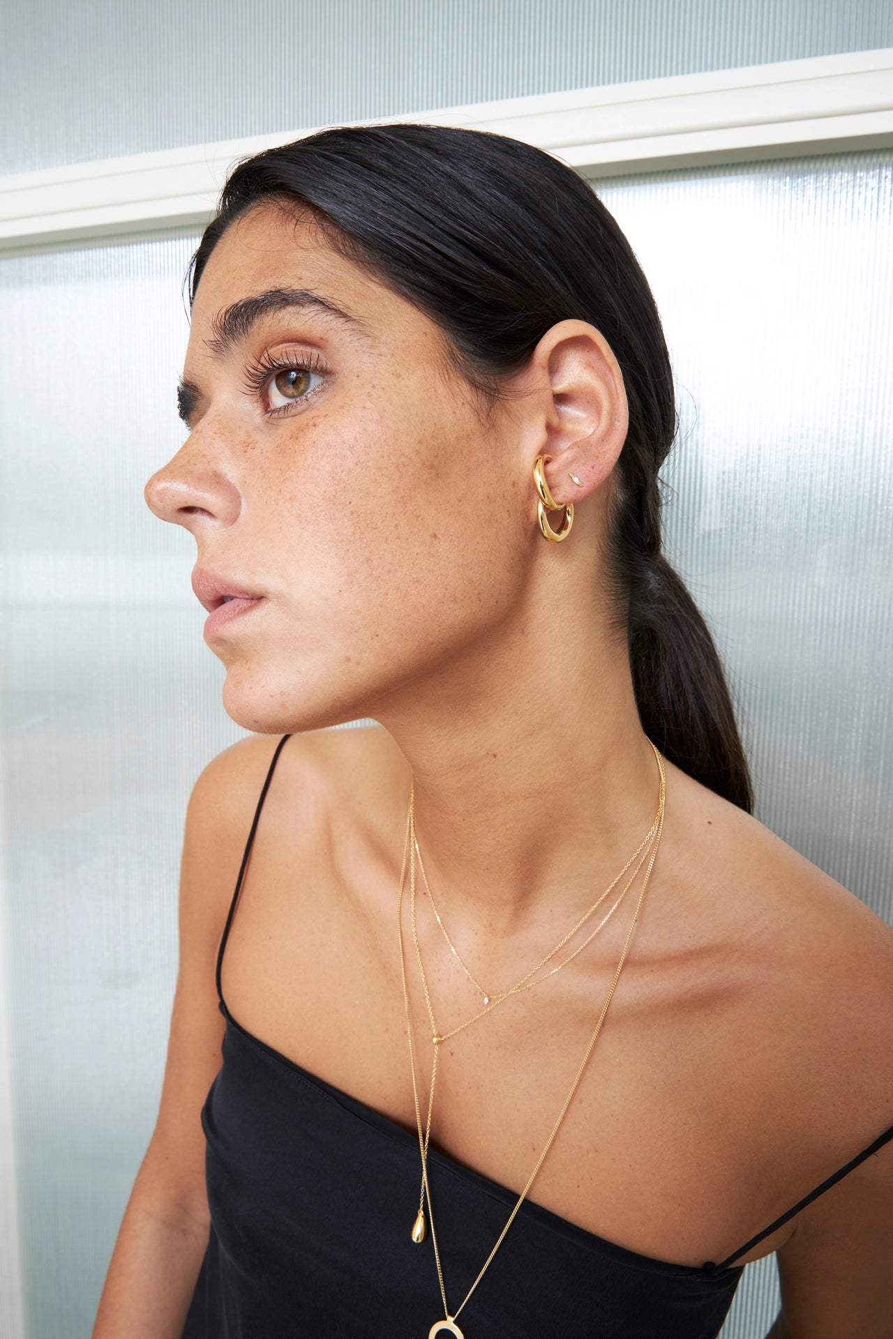 Woman wearing gold hoop earrings and a necklace against a neutral background