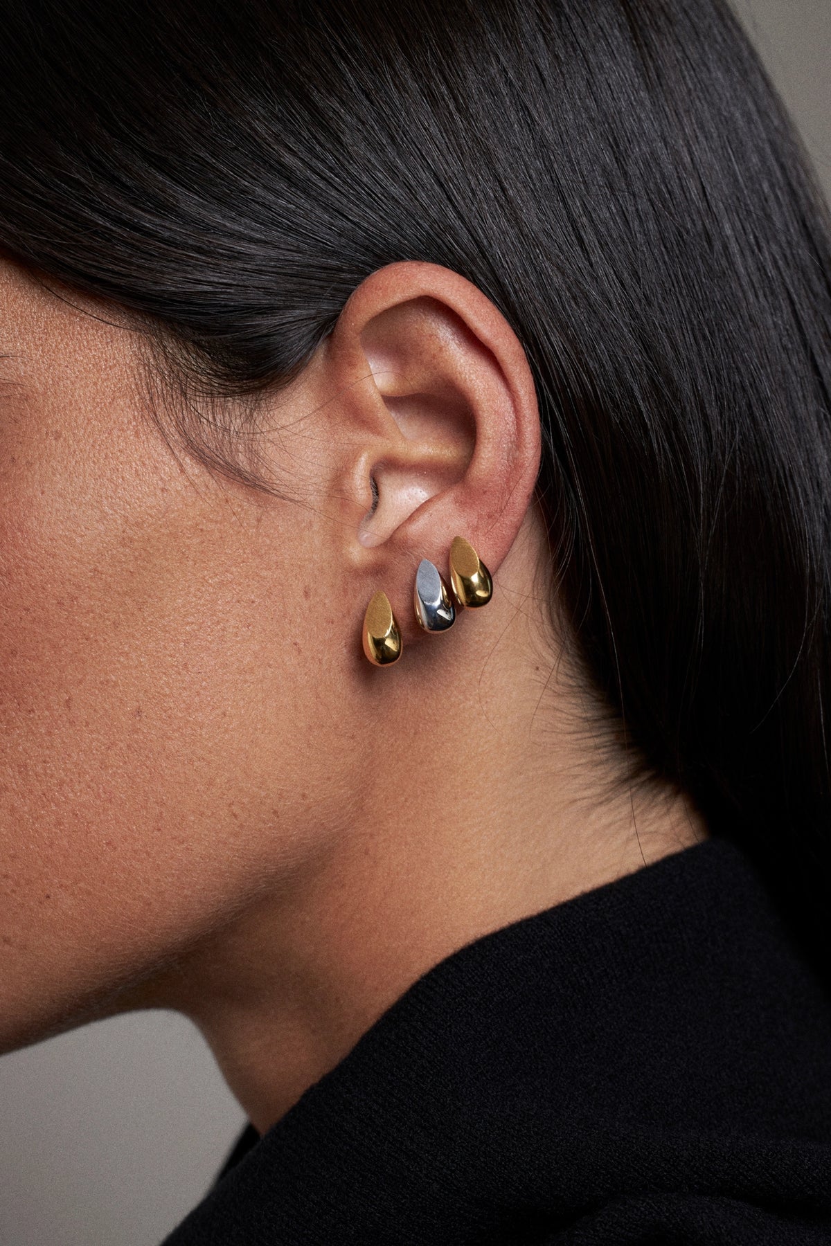 CINCO teardrop earrings worn on ear, showcasing gold and silver finishes.