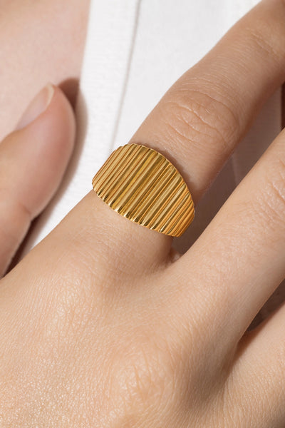 Textured fluted signet ring Cannelé in gold tone worn on a finger, showing its wide oval face and vertical ribbed texture.